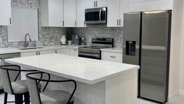 Une cuisine moderne dotée d’un îlot central, d’appareils électroménagers en acier inoxydable et de luminaires suspendus.