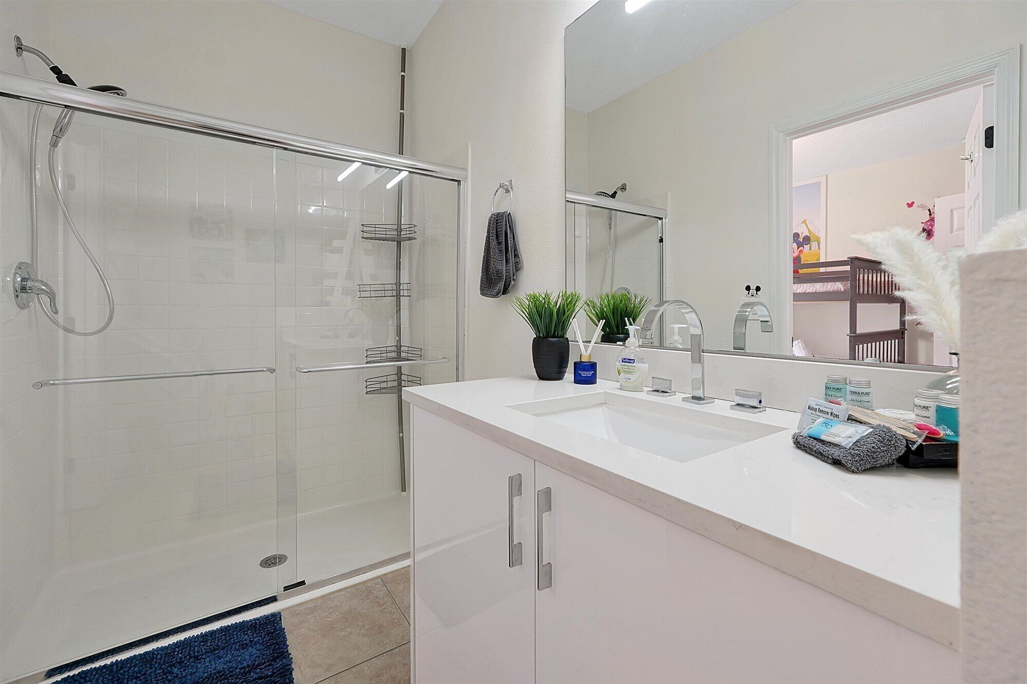 A modern bathroom with a glass shower enclosure, a white sink with a mirror, and a small potted plant.