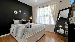 Quarto com cama, abajures, um espelho grande e uma janela com cortinas.