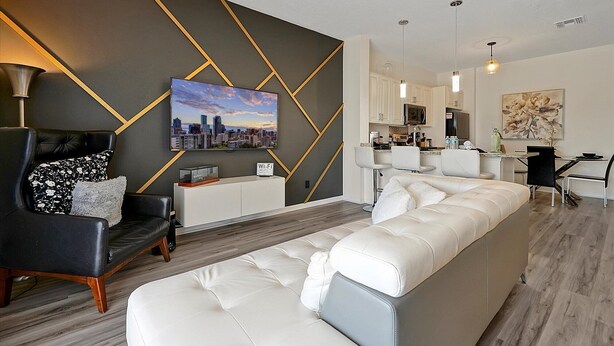 Uma sala de estar moderna com um sofá branco, uma poltrona de couro preto e uma pintura de paisagem urbana na parede.