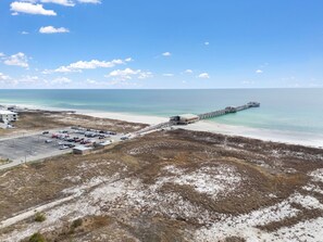 A beach with a pier extending into the ocean, a parking lot, and a building on the left. - 🌞Condo in Gulf Shores on 3rd Floor-Sea Glass-316🌞 (Gulf Shores)