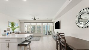 Une cuisine moderne dotée d’un îlot central, d’un coin repas avec une longue table et des chaises, et d’une grande fenêtre offrant une vue sur la ville.
