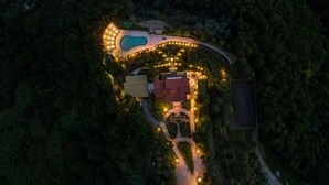 Vista aérea de un resort con piscina, un edificio central y un camino bien iluminado.