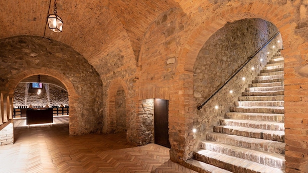 An interior with stone arches, a wooden herringbone floor, and a staircase with stone steps.