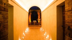 A corridor with wooden walls and a brick floor, leading to a dining area with tables and chairs.