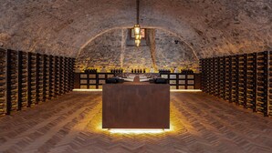 An underground wine cellar with stone walls, wooden wine racks, and a central wooden counter.