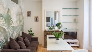 A modern living room with a brown sofa, a white dining table, and a TV on a white stand. There are glass shelves above the TV and a large mirror on the wall. - 2 Pièces Quartier Rue du Commerce, Proche Tour Eiffel (Paris)