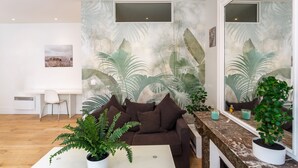 A modern living room with a brown sofa, a white coffee table, and a large mirror. There is a desk with a chair and a potted plant. - 2 Pièces Quartier Rue du Commerce, Proche Tour Eiffel (Paris)