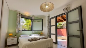 Ein Schlafzimmer mit Bett, Nachttisch, Lampe, Fenster mit Vorhängen, Spiegel und einer Schiebeglastür zu einem Außenbereich.