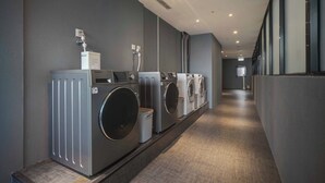 A laundry facility with multiple washing machines and dryers, a ventilation system, and a grey carpeted floor. - Fun Stay Inn Ximen (Taipei)