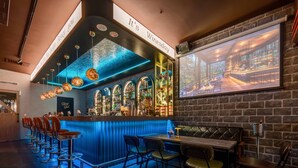 A bar area with a blue-lit bar counter, multiple stools, and a projection screen displaying a bar scene. - Fun Stay Inn Ximen (Taipei)