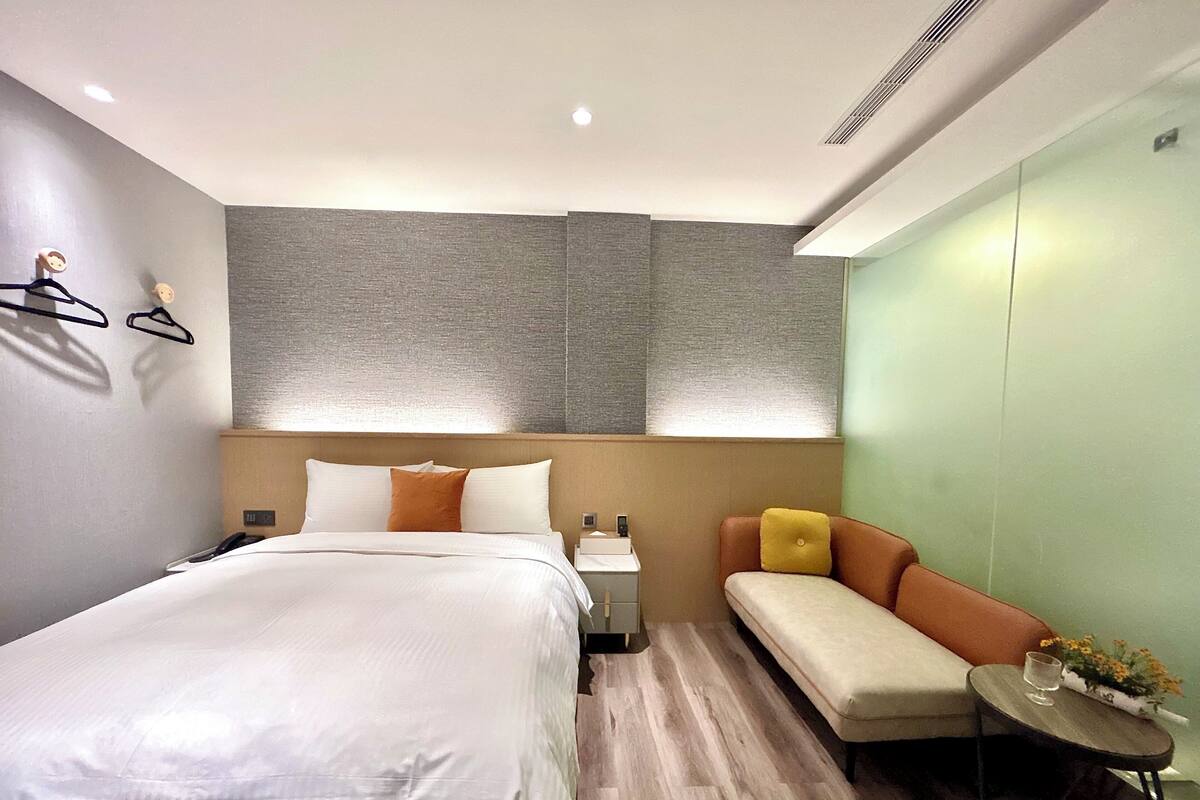 Een moderne hotelkamer met een groot bed, een bank, een kleine tafel met een bloemenvaas, en een wandlamp.