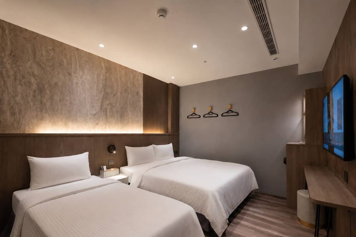 Een moderne hotelkamer met twee bedden, een grote tv aan de muur en een houten bureau.