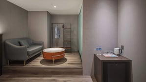A modern hotel room with a grey sofa, a round orange ottoman, a small kitchenette with a coffee maker, and a wardrobe with a ladder. - Fun Stay Inn Ximen (Taipei)
