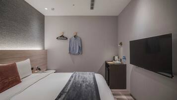 A modern hotel room with a large bed, a flat-screen TV, a desk with a coffee maker, and a wall-mounted TV.