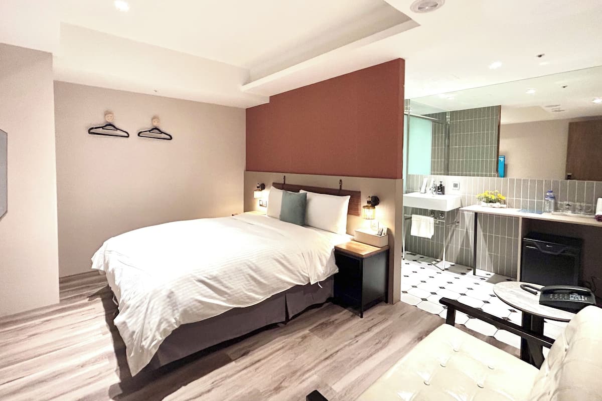Een moderne hotelkamer met een groot bed, nachtkastjes, een klein bureau en een badkamer met spiegel en wastafel.