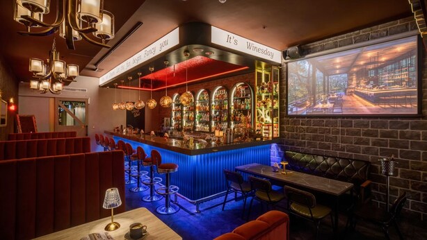 A bar area with a red-lit bar counter, multiple hanging lights, and a projection screen displaying a scenic view. - Fun Stay Inn Ximen (Taipei)