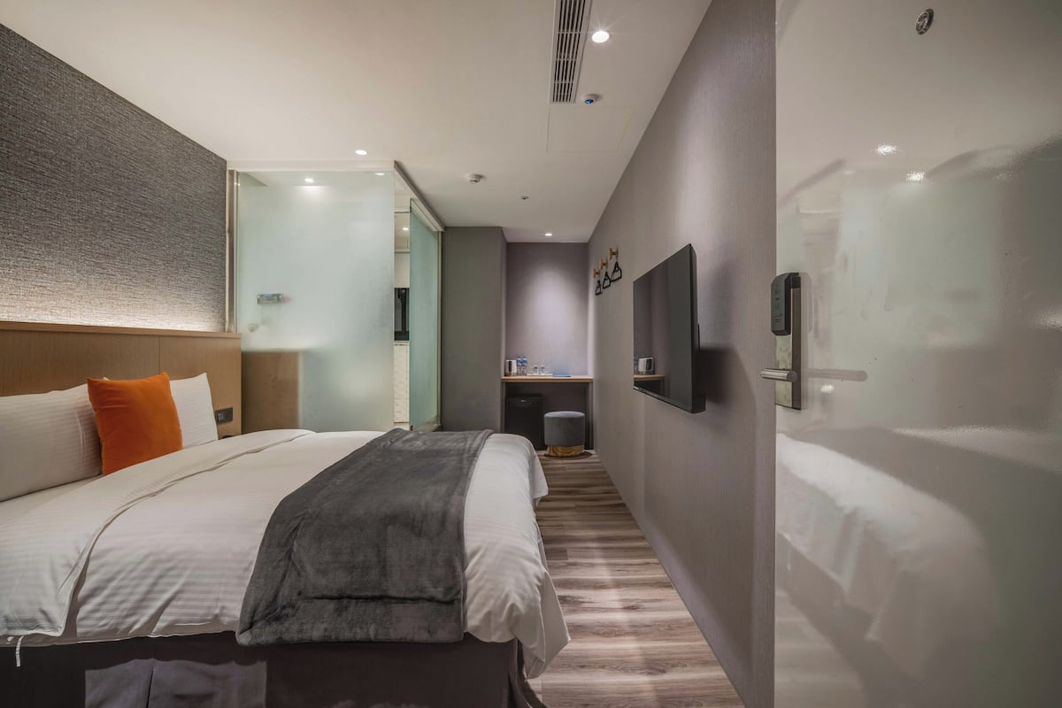 Een moderne hotelkamer met een groot bed, een nachtkastje, een bureau en een spiegel.