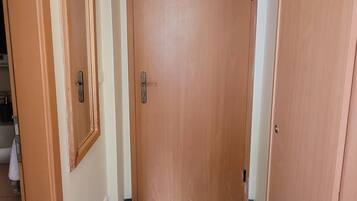 A hallway with two wooden doors, a small mirror on the left wall, and a dark carpeted floor.