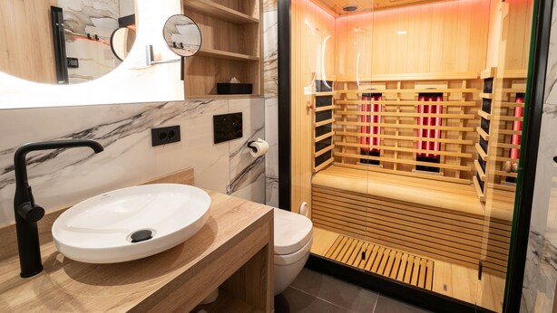 Une salle de bain moderne avec un pare-baignoire en marbre, un miroir rond, un meuble-lavabo en bois, un lavabo blanc et un sauna à parois de verre.