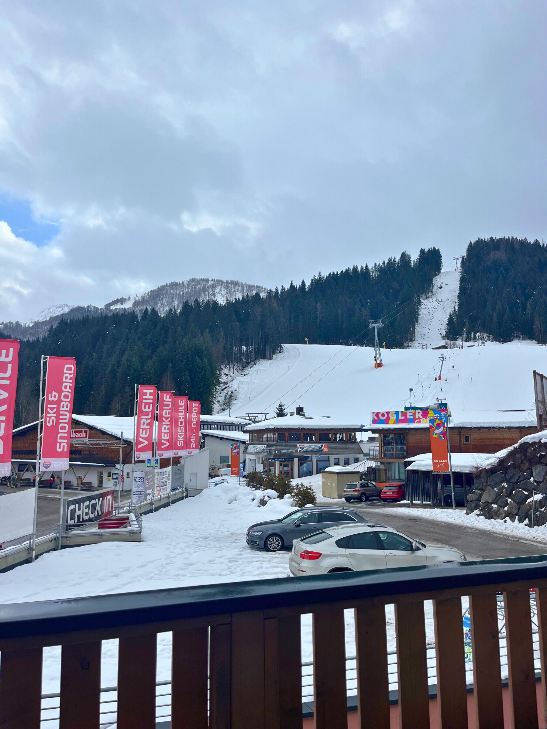 A ski resort with a check-in area, ski and snowboard rental signs, and a view of a snowy mountain.