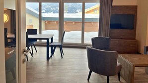 Un interior moderno con techo de madera, ventanas amplias con vistas nevadas, zona de comedor y televisor de pantalla plana en la pared.