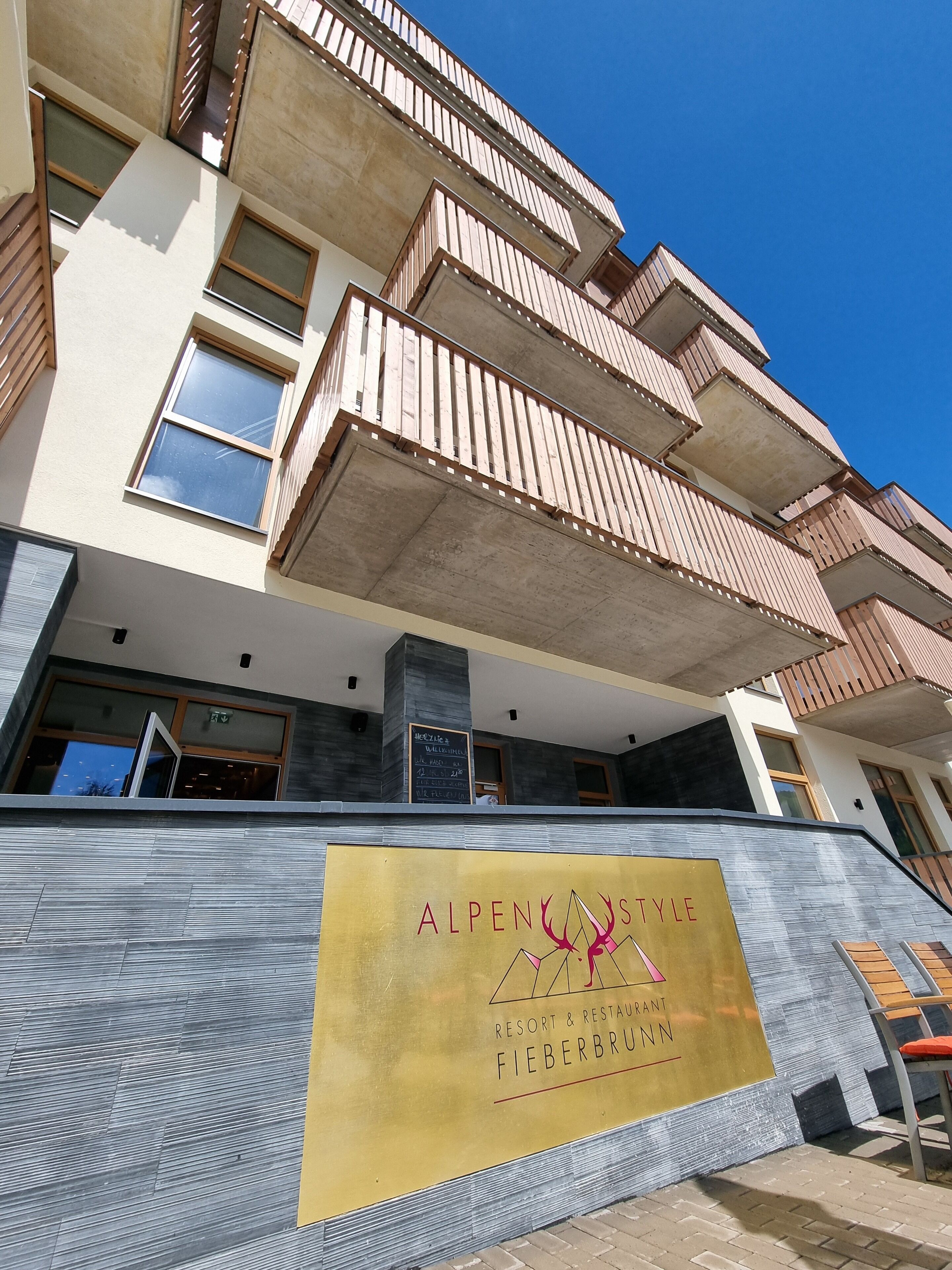 Um edifício com a placa 'AlpenStyle Resort & Restaurant' e design arquitetônico moderno, com varandas.