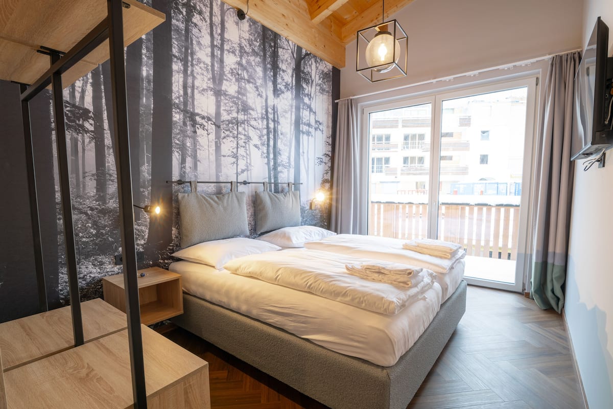 Een moderne slaapkamer met een groot bed, een houten bureau en uitzicht op de stad.