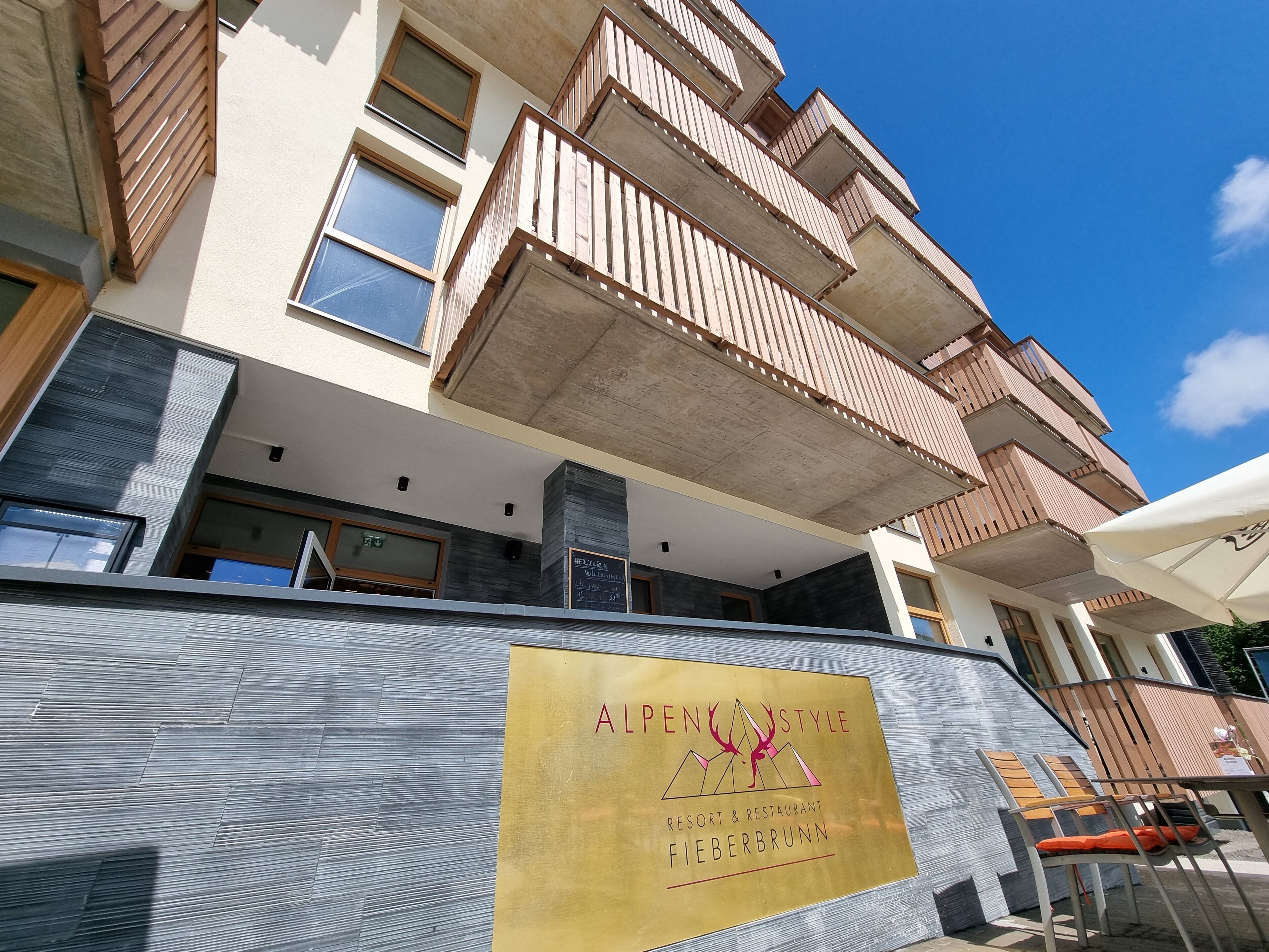 A multi-story building with balconies, a sign for 'ALPENSTYLE RESORT & RESTAURANT FIEBERBRUNN', and a modern exterior design.