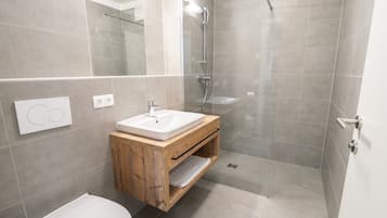 Un baño moderno con tocador de madera, lavamanos blanco, cabina de ducha de vidrio y un inodoro.