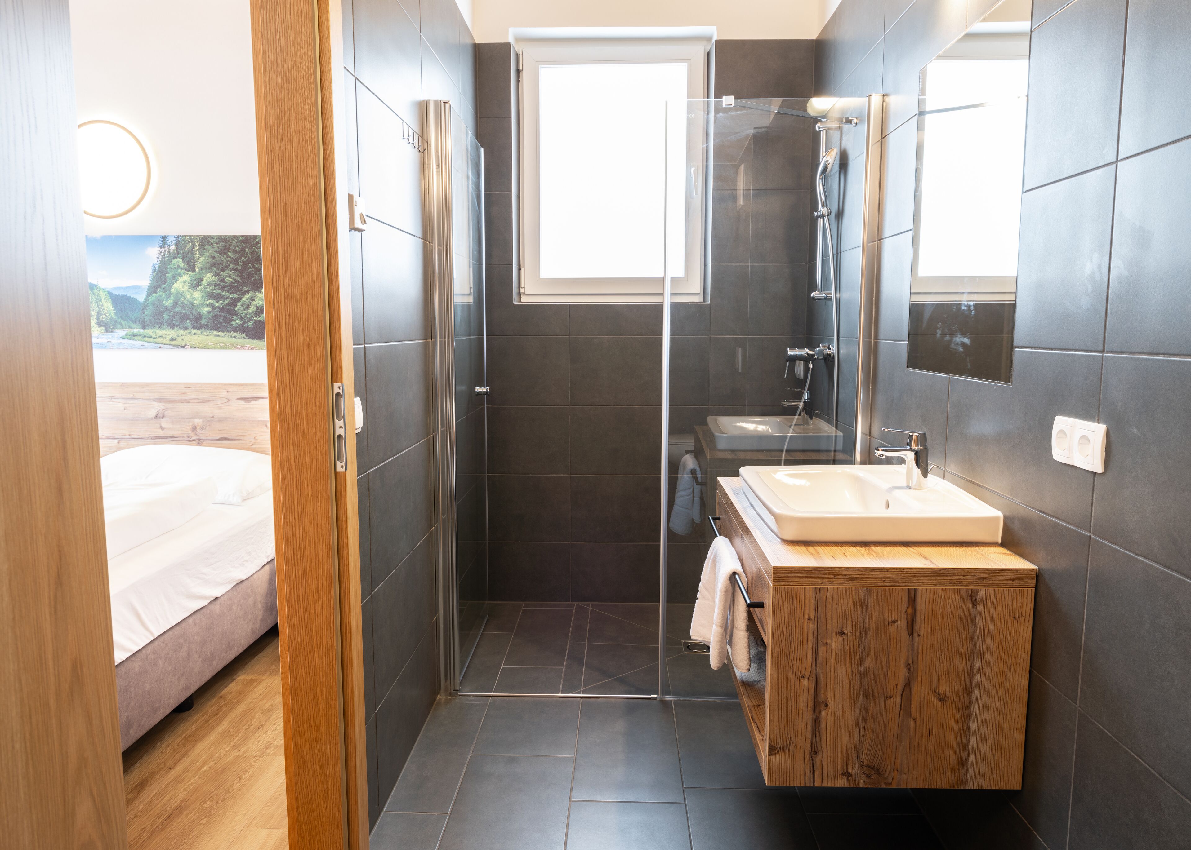 A modern bathroom with a wooden vanity, a glass shower enclosure, and a large mirror.