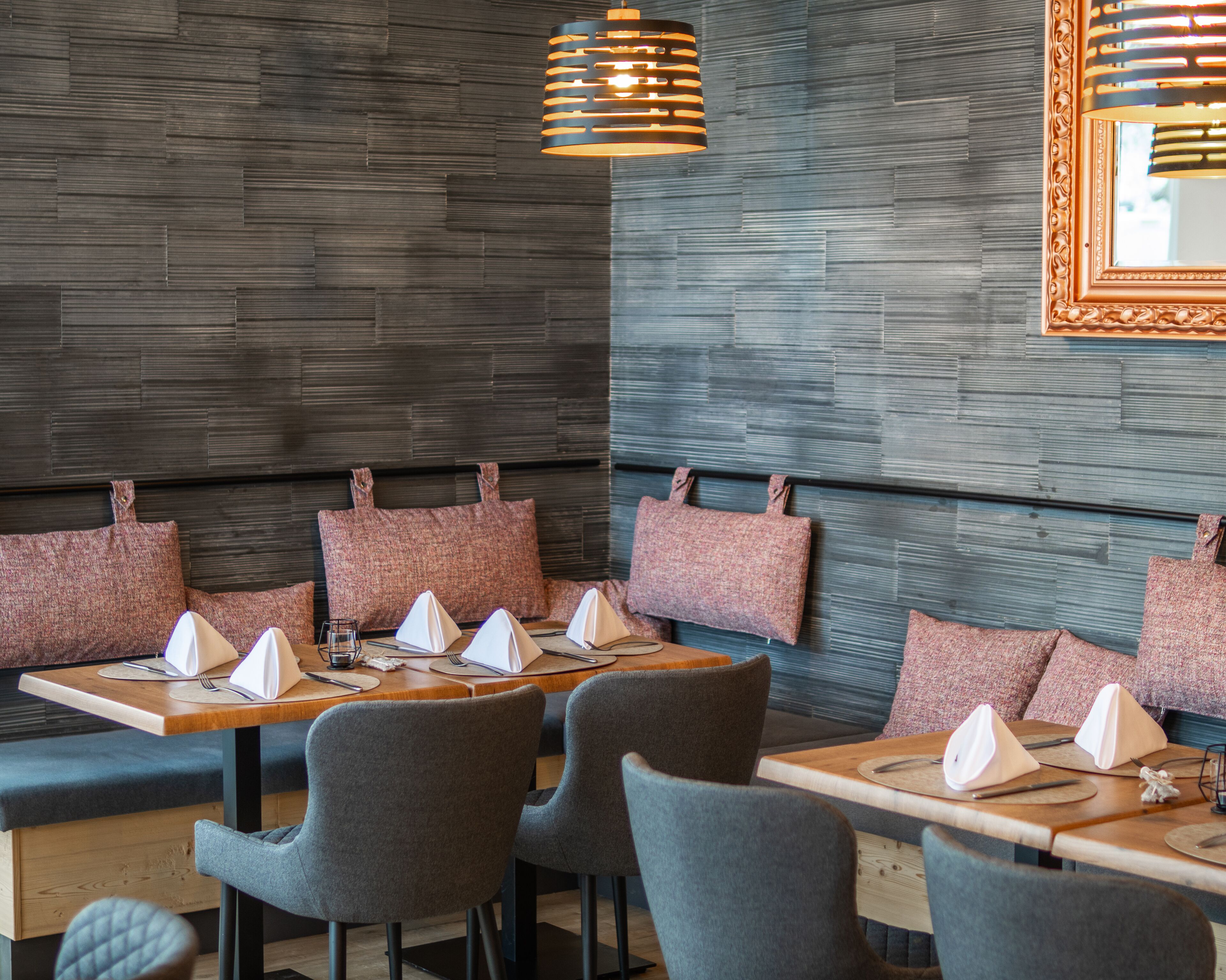 A restaurant interior with wooden tables, grey upholstered chairs, and a textured wall.