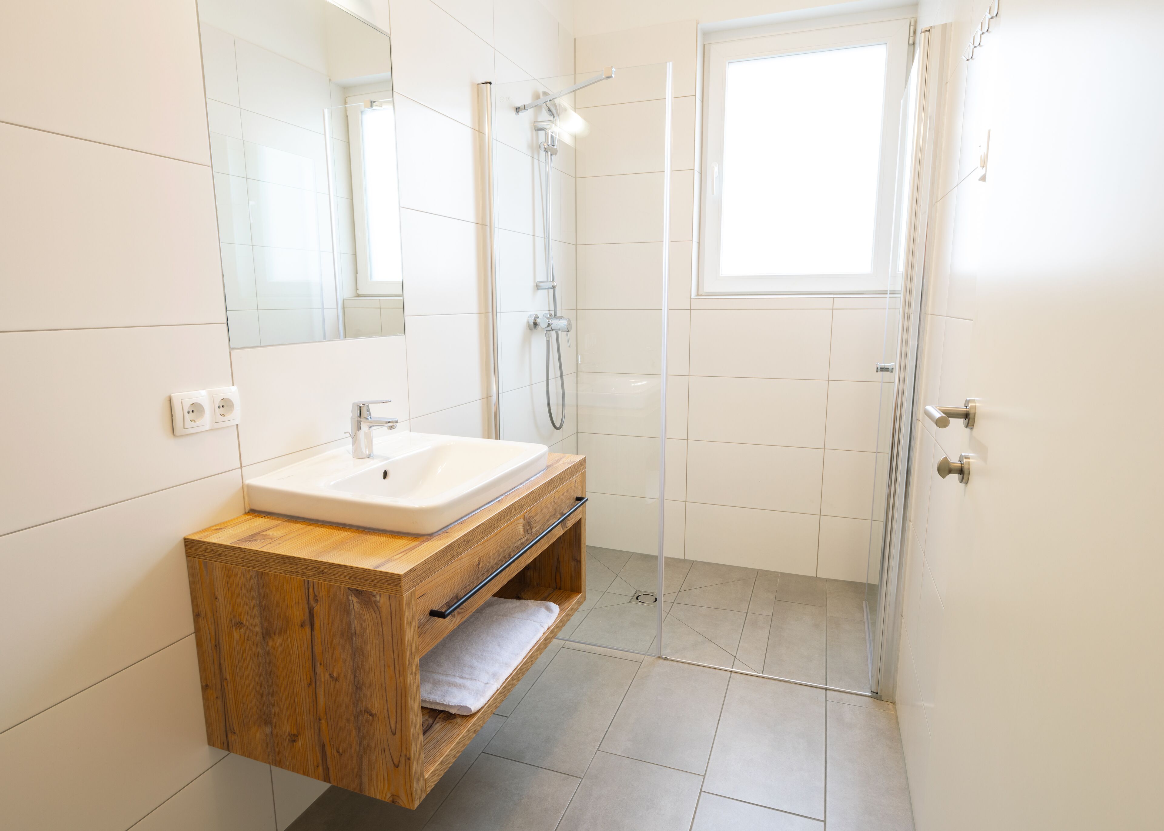 Un bagno moderno con un mobile bagno in legno, un lavandino bianco, uno sportello doccia in vetro e un grande specchio.