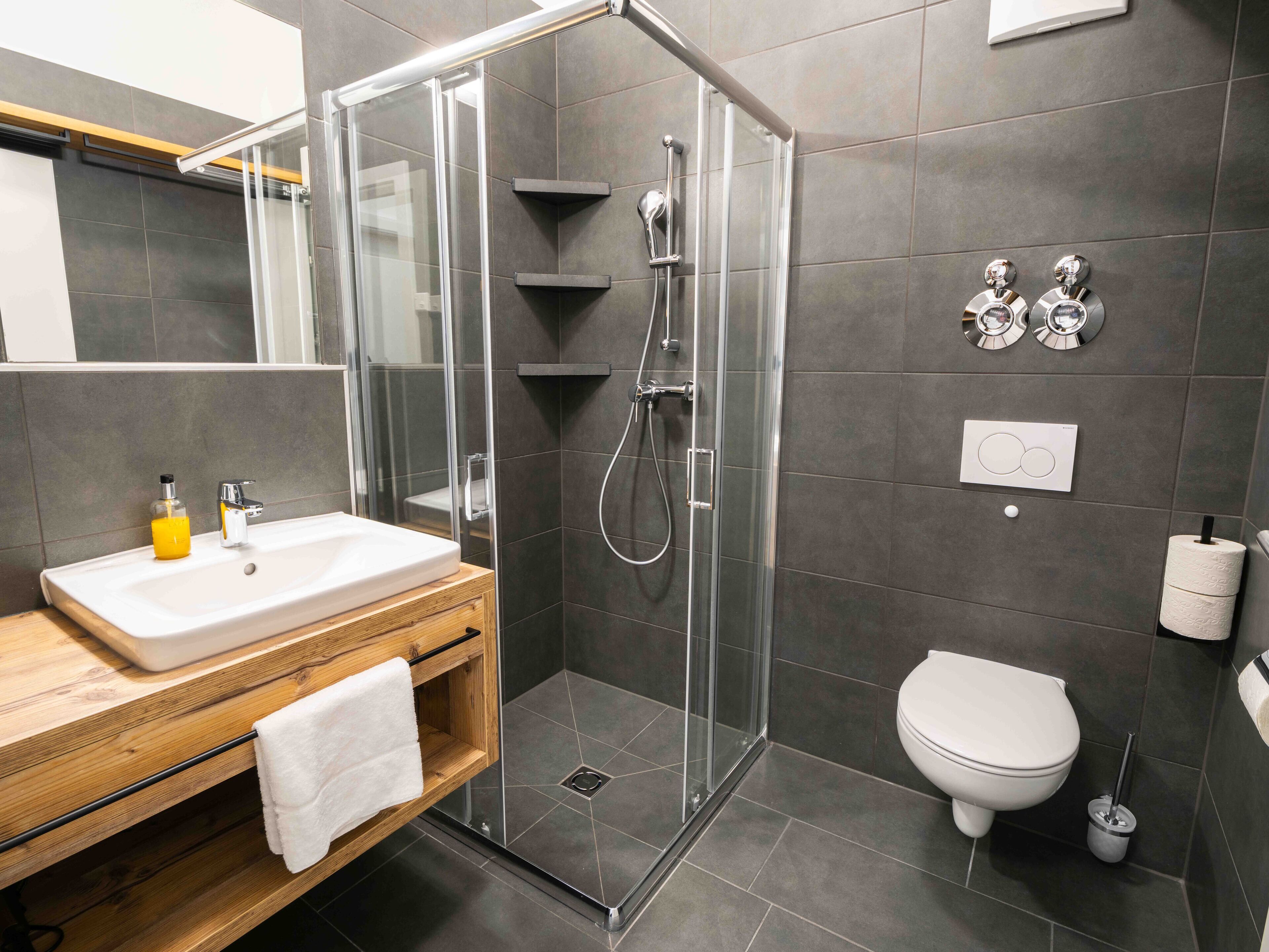 A modern bathroom with a glass shower enclosure, a wooden vanity, a toilet, and a towel rack.