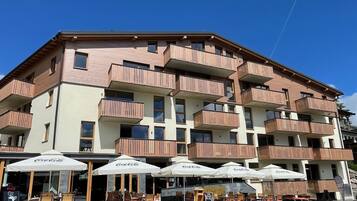 Un edificio de varios pisos con balcones, mobiliario exterior con sombrillas y un cartel de Coca-Cola.