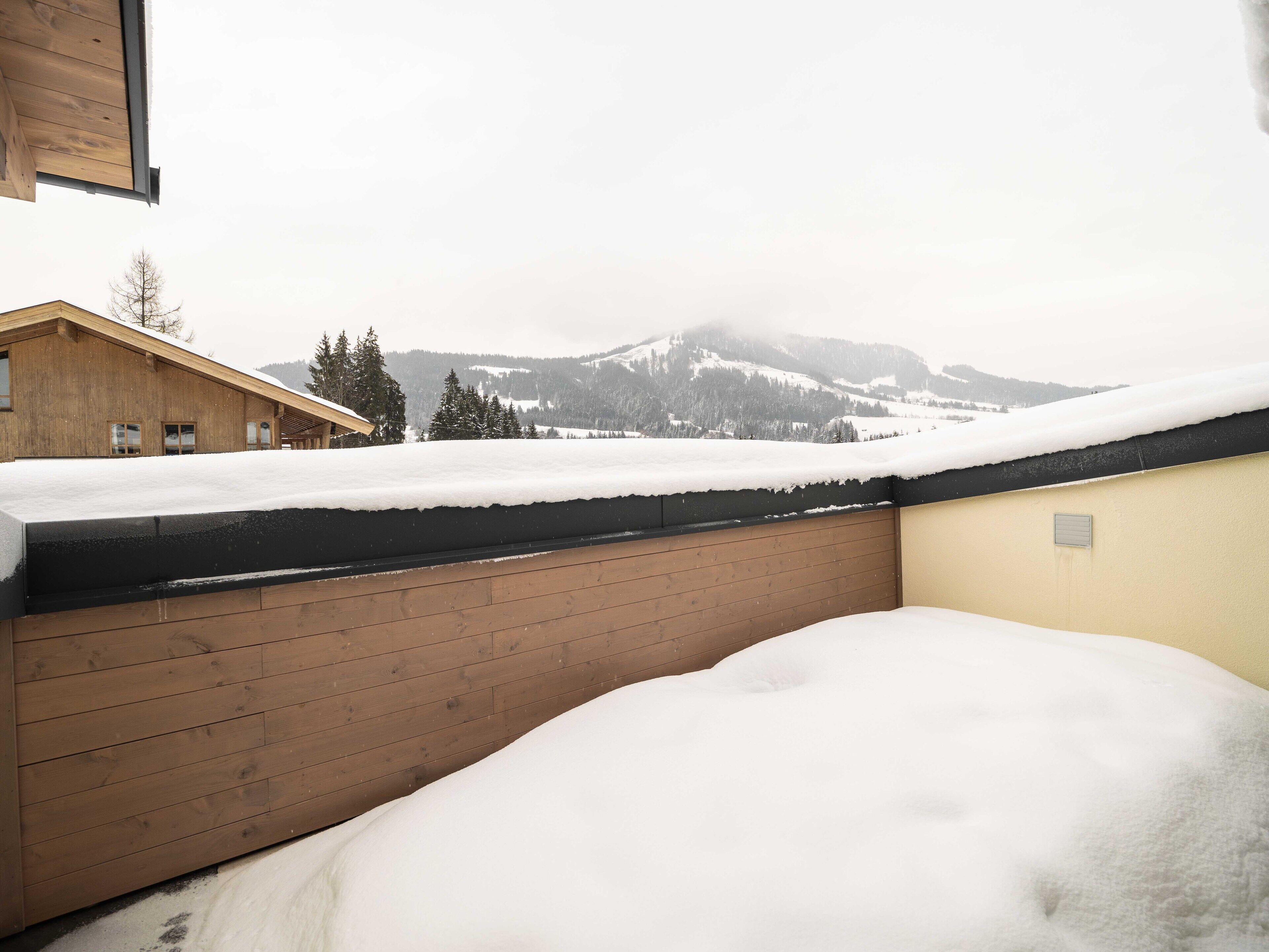 A wooden building with a snow-covered roof and a view of snow-covered mountains in the background.