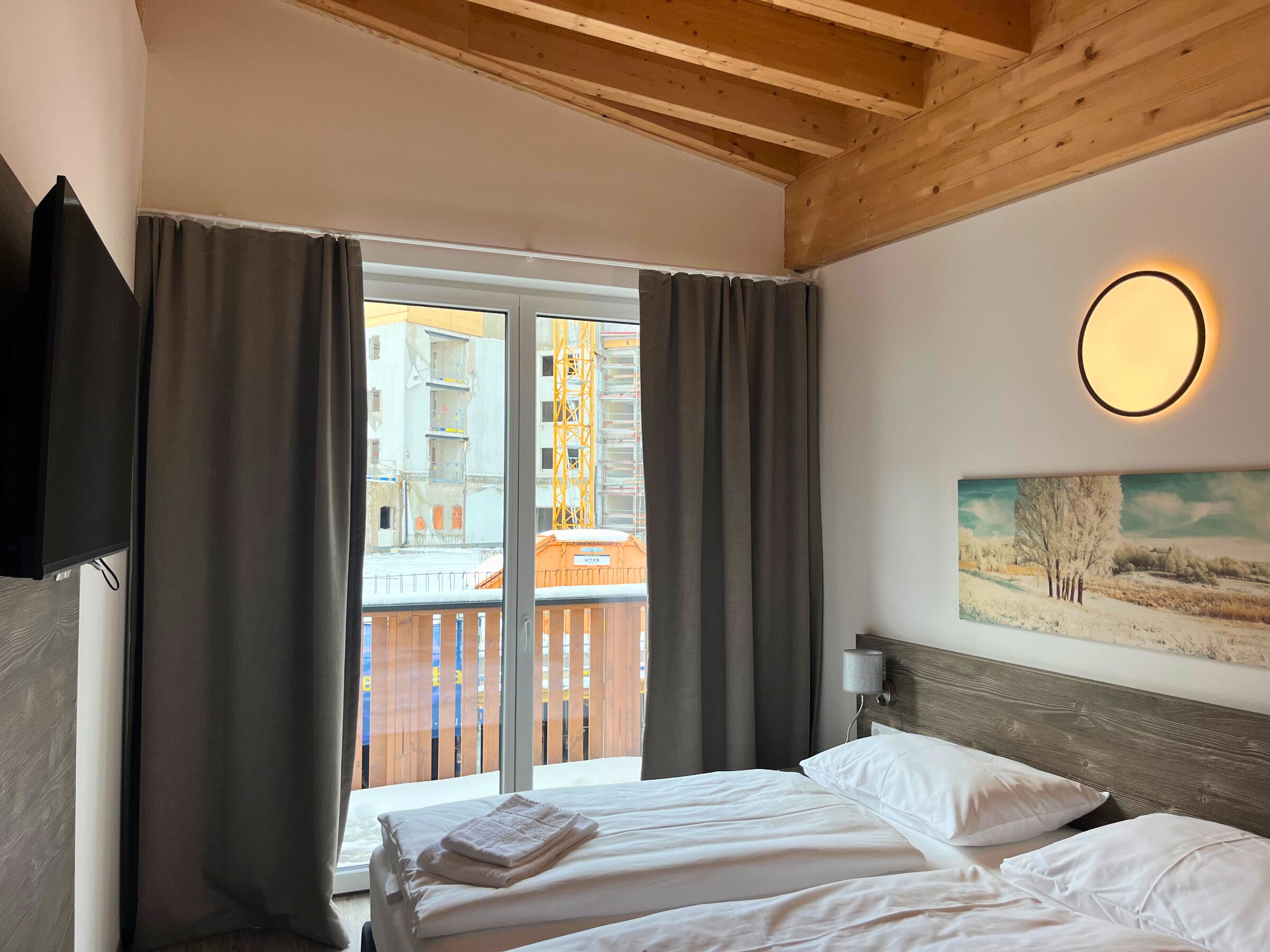 A hotel room with a bed, a painting on the wall, and a view of a building through the window.