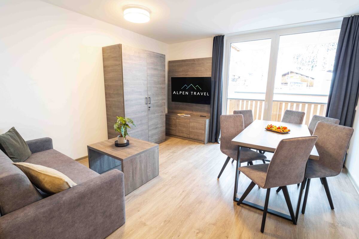 Een moderne woonkamer met een bank, een salontafel met een plant, een eethoek met een tafel en stoelen, en een televisie aan de muur.