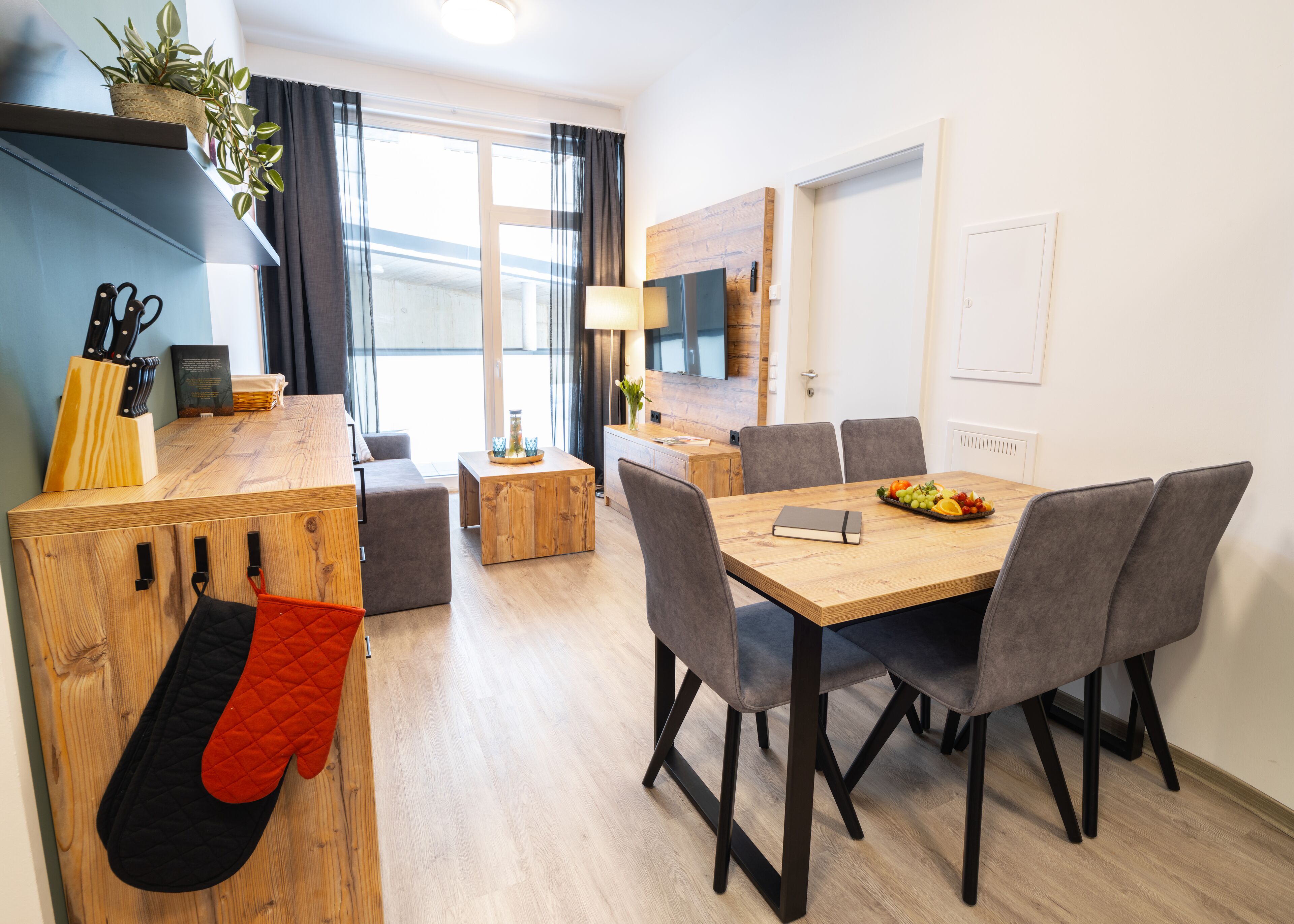 A modern kitchen with wooden cabinetry, a dining table with chairs, and a kitchen island with a plant and utensils.