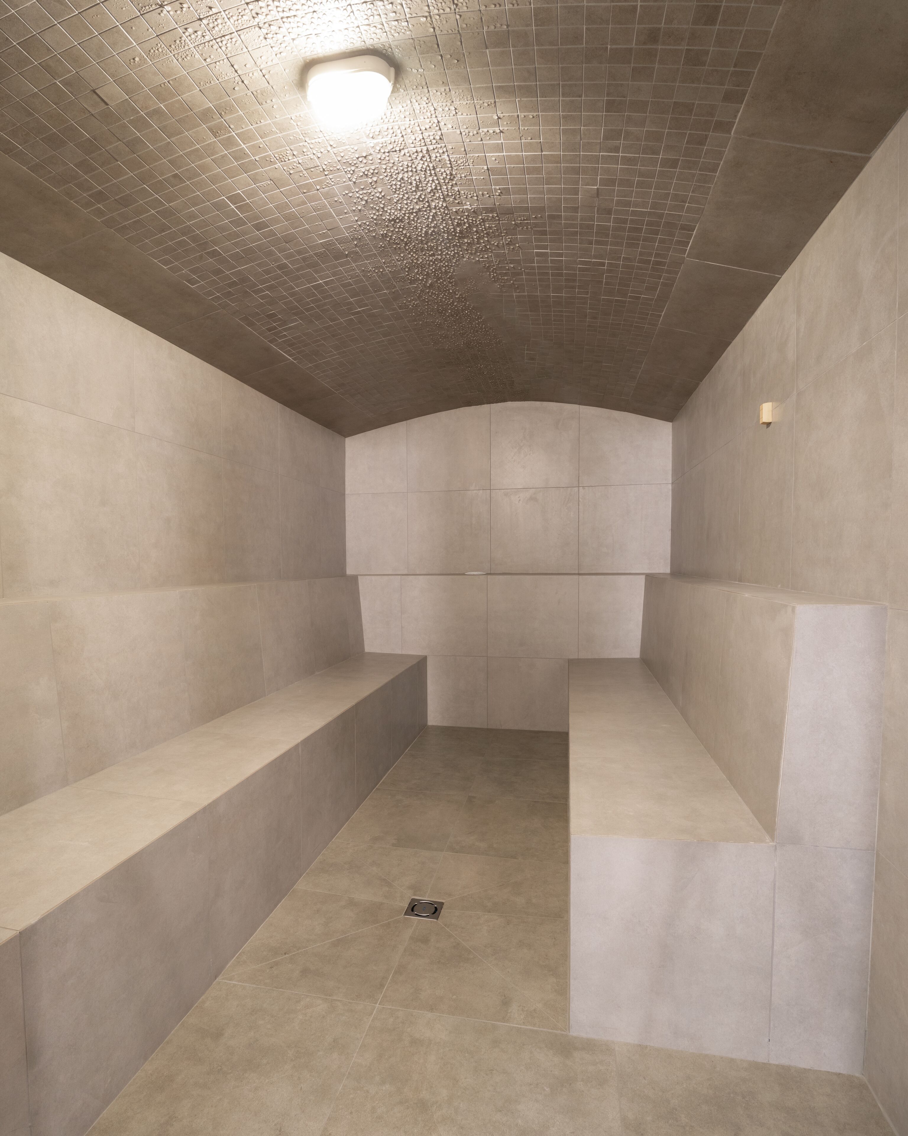 A modern, minimalist bathroom with a tiled floor and walls, a built-in bench, and a ceiling light fixture.