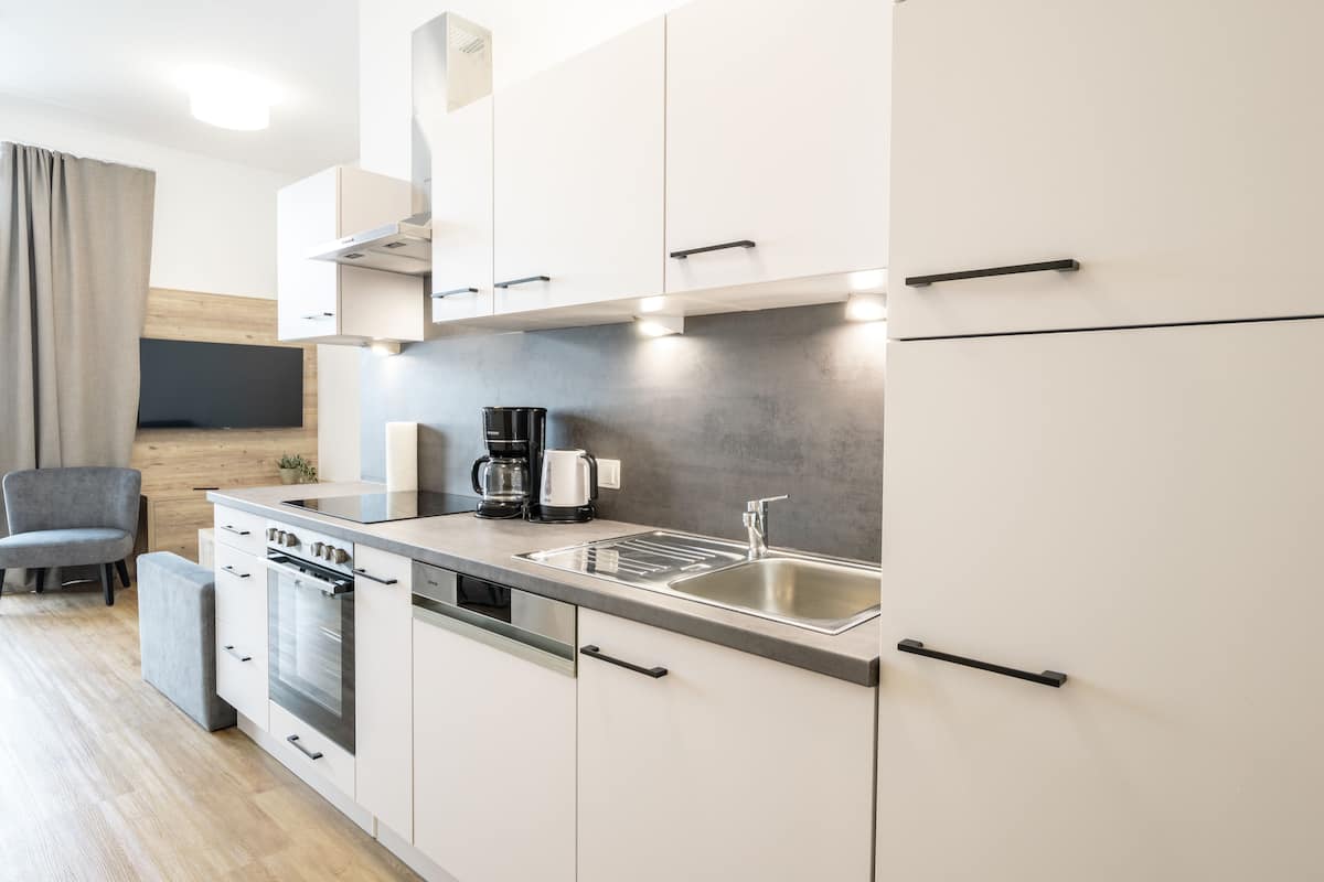Een moderne keuken met witte kasten, een roestvrijstalen spoelbak, een koffiezetapparaat en een vaatwasser.