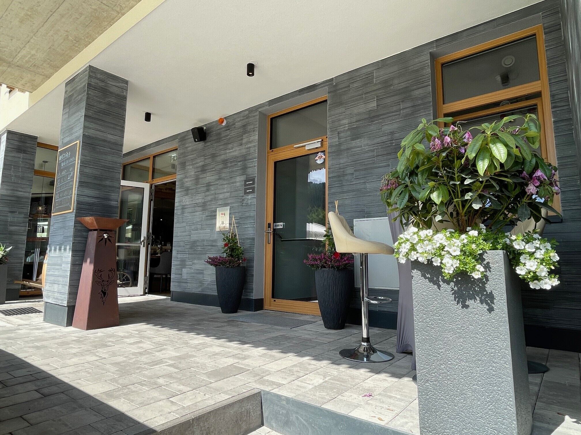 A modern building with a glass entrance, a metal sculpture, and potted plants.