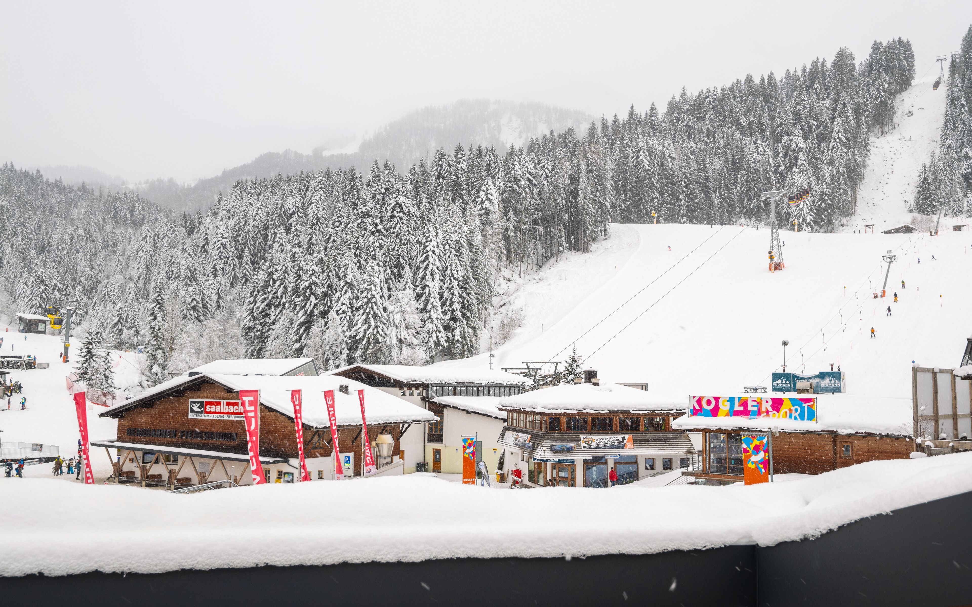 A ski resort with buildings, a ski lift, and snow-covered trees.