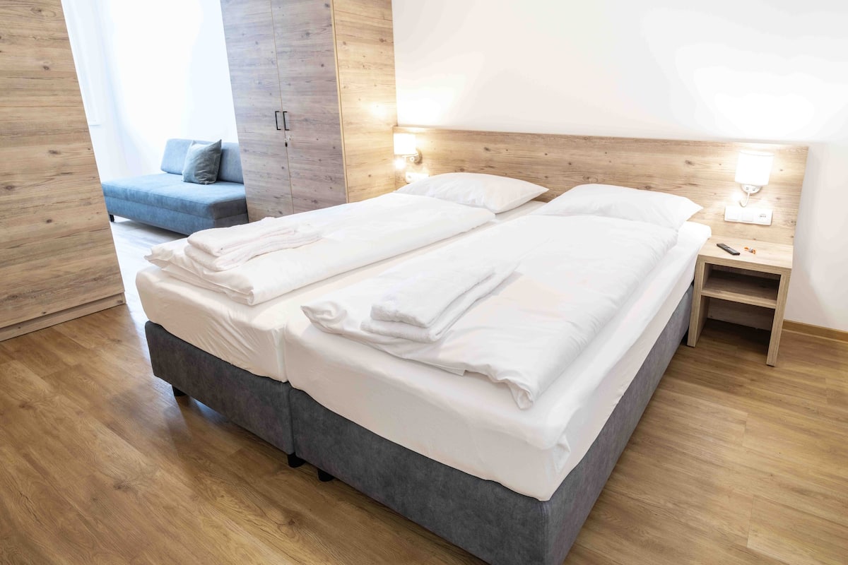 Een moderne hotelkamer met een groot bed, een kast, een nachtkastje met een lamp en een bank op de achtergrond.