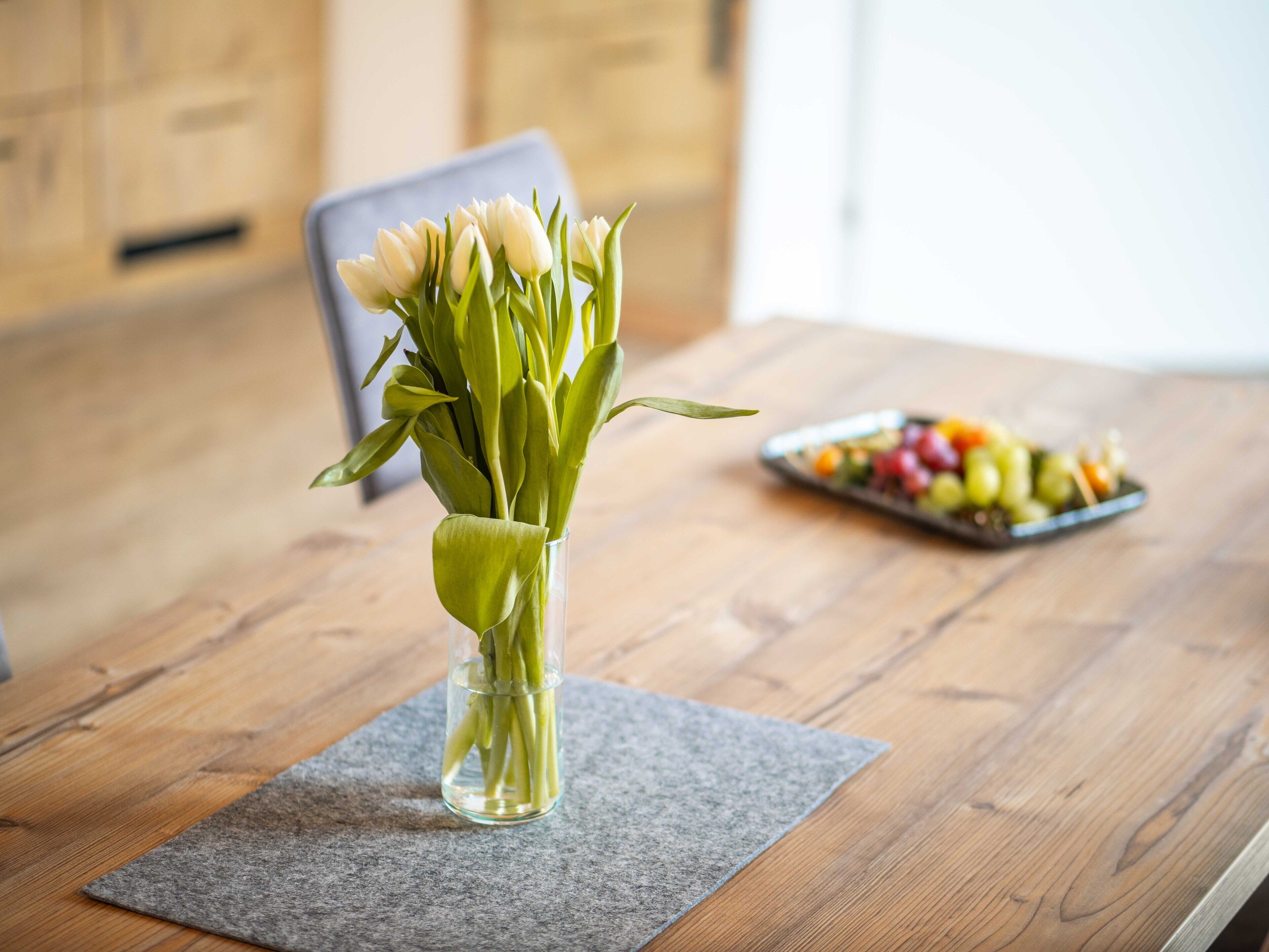 A wooden table with a vase of white flowers and a fruit platter.