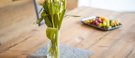 A wooden table with a vase of white flowers and a fruit platter.