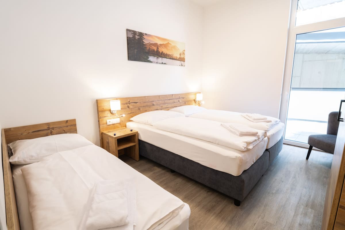 Een hotelkamer met twee bedden, een houten hoofdbord, bedlampjes, een schilderij en uitzicht door een groot raam.