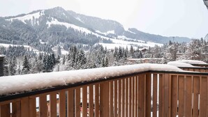 Un balcón de madera con barandas cubiertas de nieve que da a un paisaje montañoso nevado.