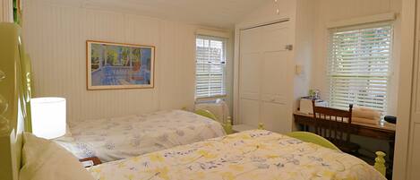 A bedroom with two beds, a ceiling fan, a painting on the wall, and a window with blinds.