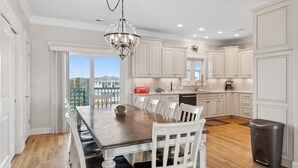 A modern kitchen with white cabinetry, a wooden dining table, and a chandelier. - Discover Oak Island Nest Egg: a spacious 5-bedroom retreat with ocean views and private pool. (Oak Island)